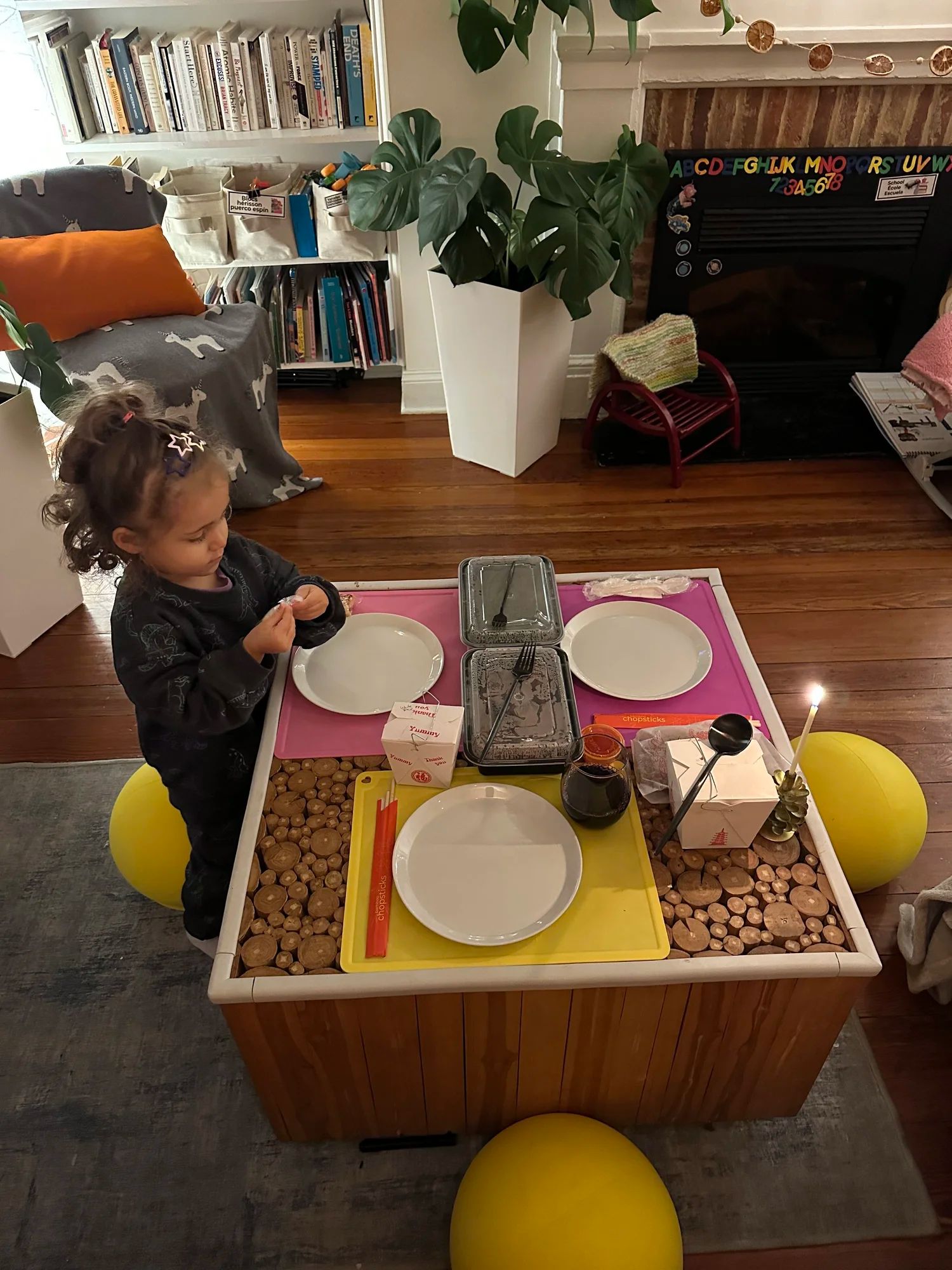 A toddler at a coffee table set for dinner with BOUNCE balls as seats