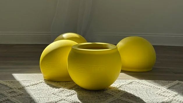 Four yellow BOUNCE balls in afternoon sun on a woven rug