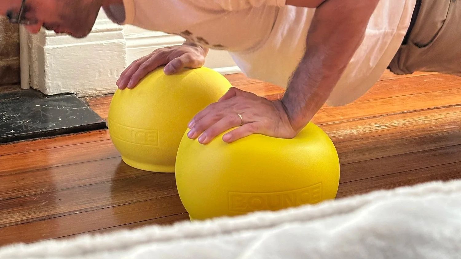 Push-ups on two yellow BOUNCE balls on a hardwood floor